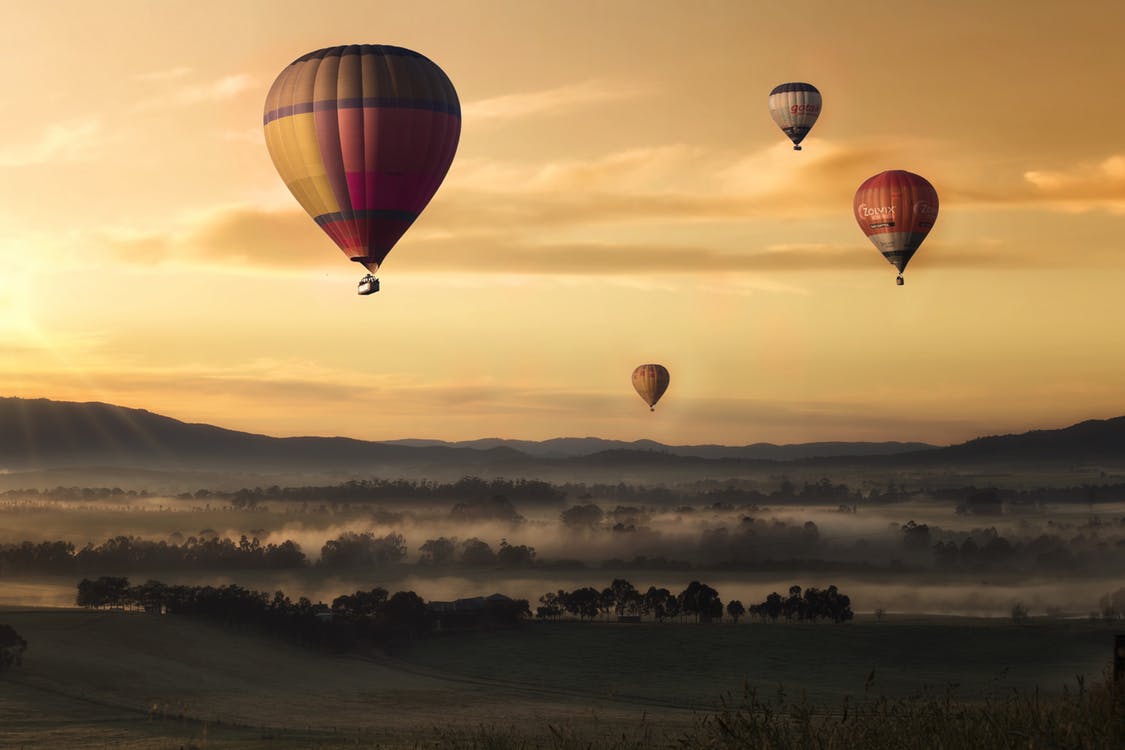Wide shot of four hot air balloons flying over grassy plains